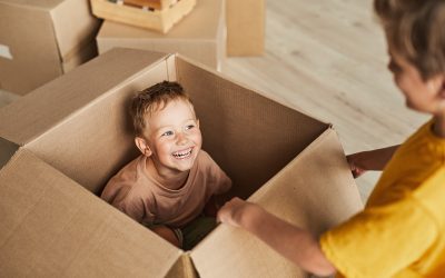 High angle portrait of happy smiling boy sitting in cardboard boxes and playing with mom in new house, copy space